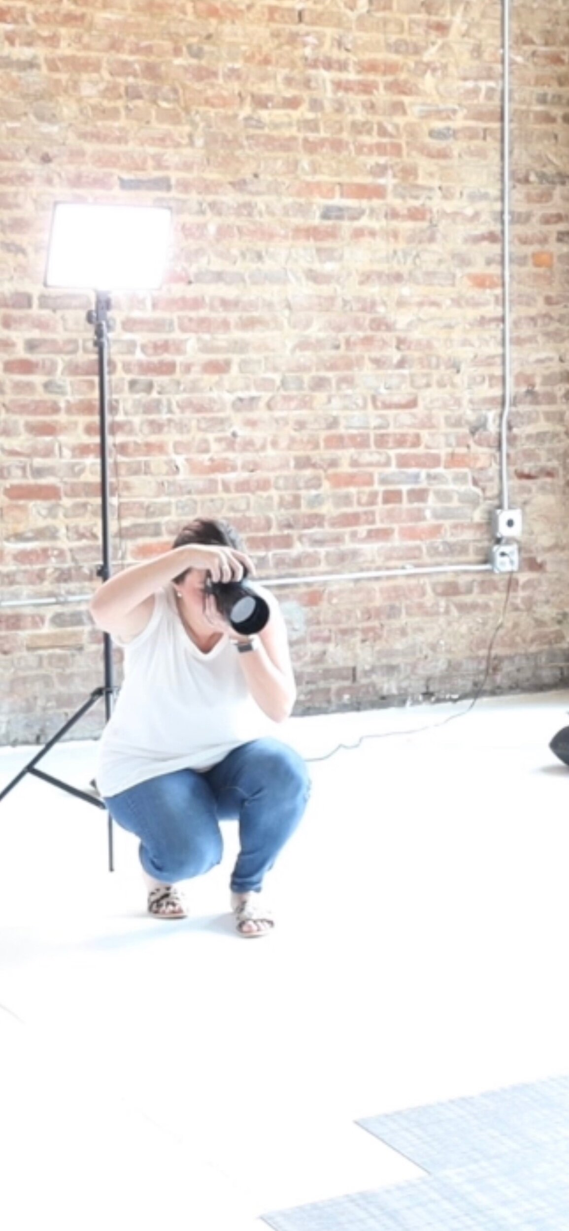 photographer with white top and jeans in a photography studio with brick wall